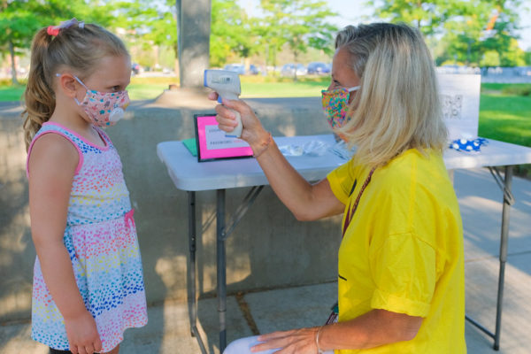 Child in a mask gets her temperature taken