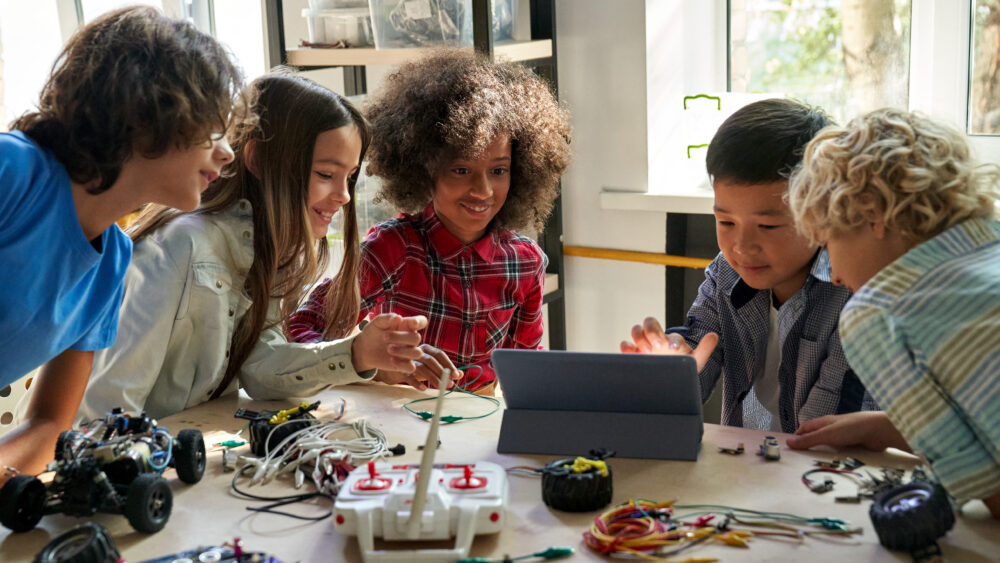 Happy diverse school children students building robotic cars using computer.