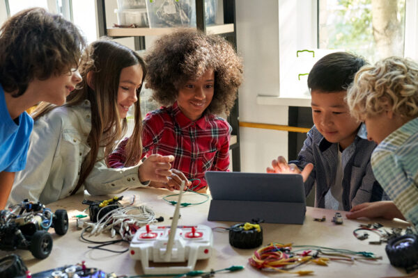 Happy diverse school children students building robotic cars using computer.