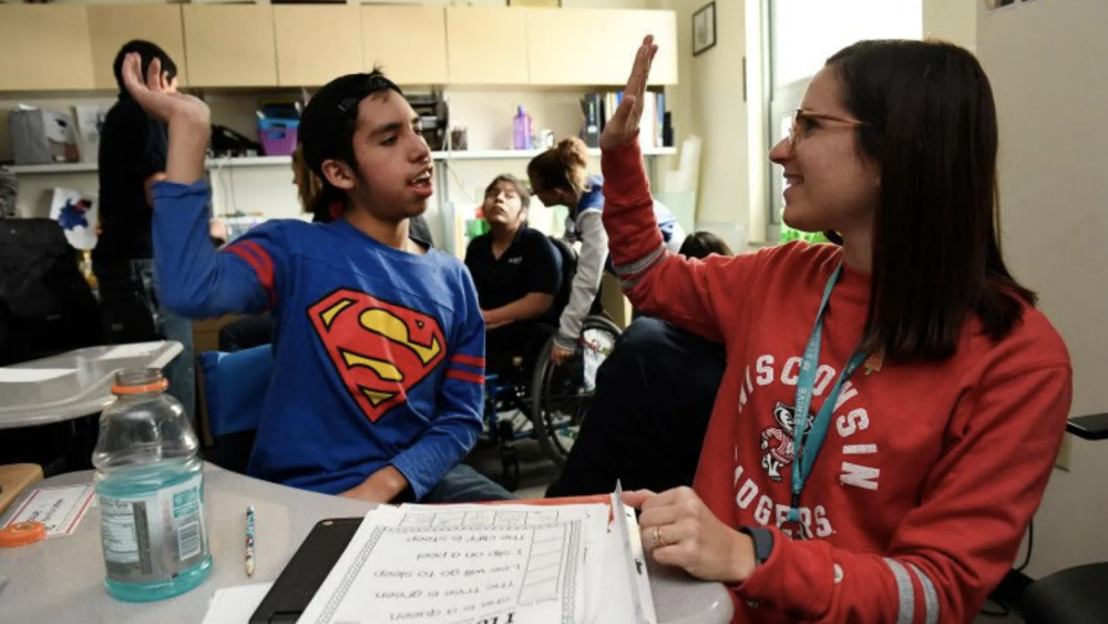 Female teacher in red shirt giving a male student in a Superman shirt a high five.