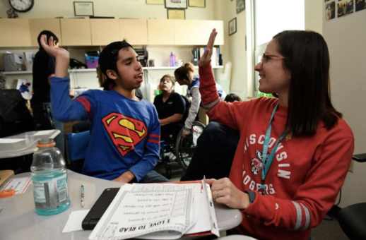 Female teacher in red shirt giving a male student in a Superman shirt a high five.