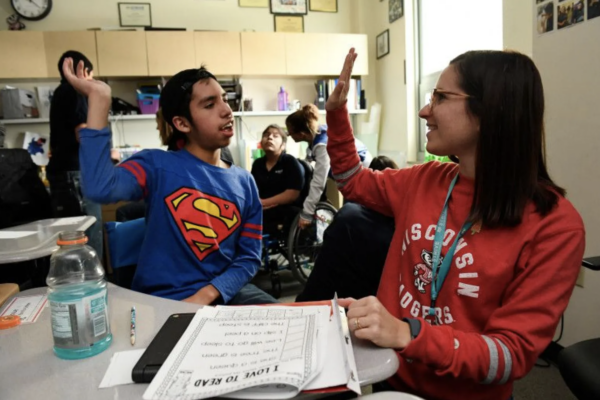 Female teacher in red shirt giving a male student in a Superman shirt a high five.