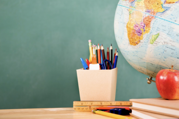 Green chalkboard with a globe, cup of pencils, books, and apple on a desk.