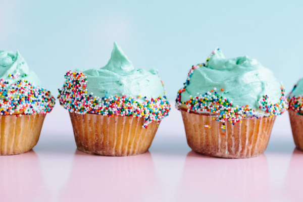 A line of cupcakes with aquamarine frosting and sprinkles against a pink and blue background