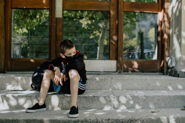 student sitting on step outside of school with mask on