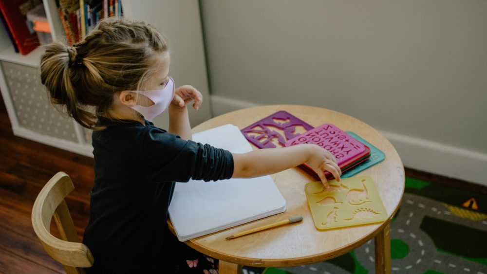 Young girl sitting at a school table wearing a face mask