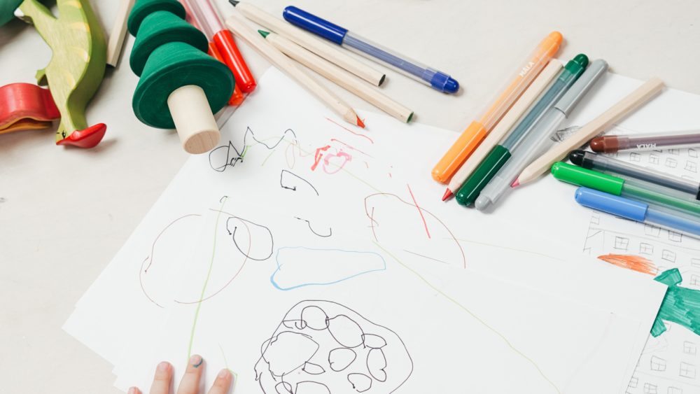 Child's hands on top of drawing, with colored pencils scattered on the table