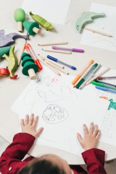 Child's hands on top of drawing, with colored pencils scattered on the table