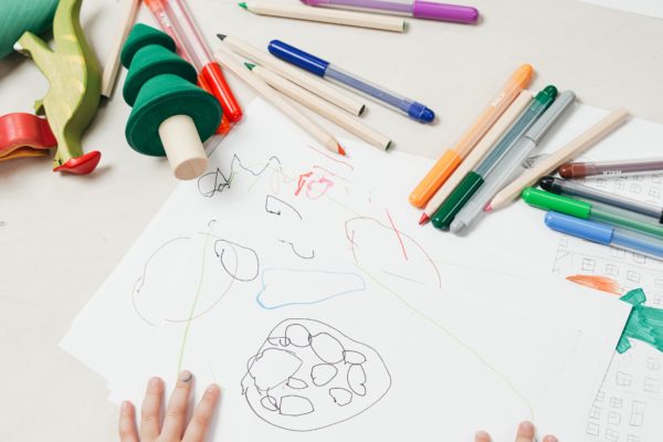 Child's hands on top of drawing, with colored pencils scattered on the table