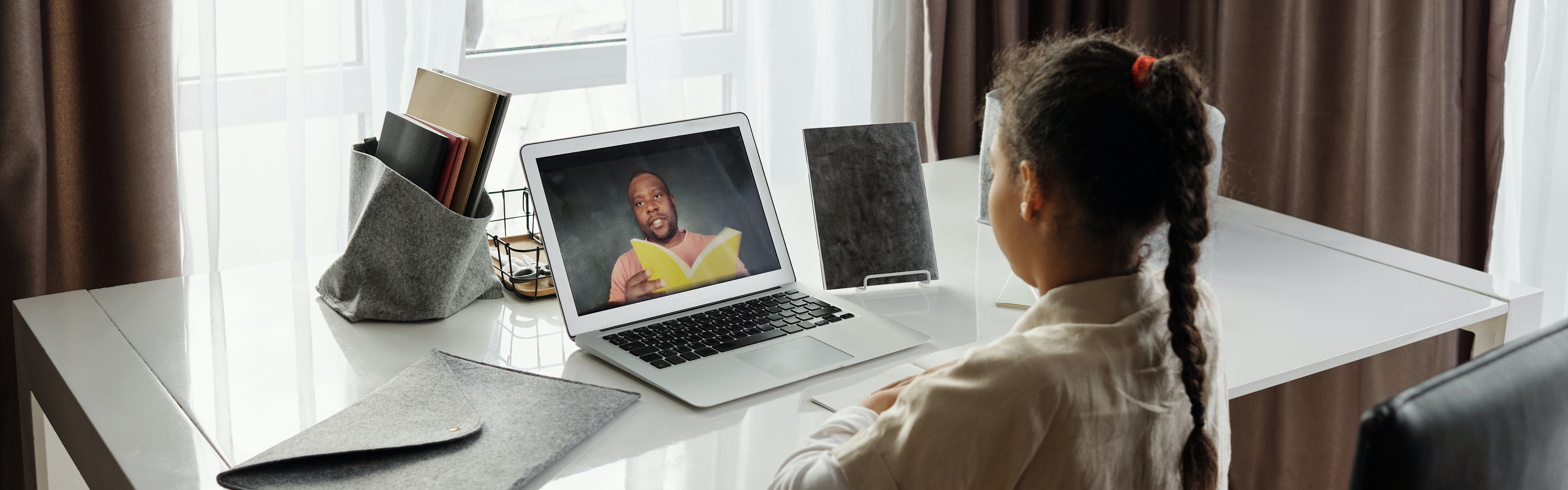 Young student watches teacher read a book over video chat