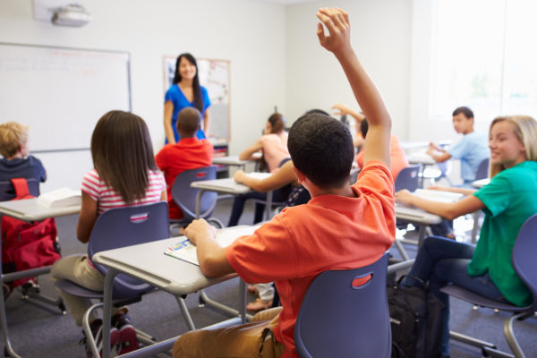 Student raising hand while sitting at a desk in a school classroom